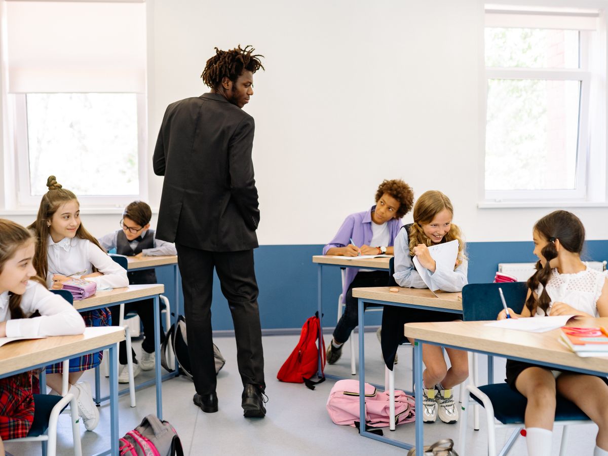A teacher watching over pupils as they work together in a bright, modern classroom
